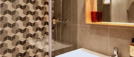 Une salle de bain moderne avec une douche à parois de verre, un lavabo blanc et un meuble en bois, ainsi qu’un mur orné d’un motif géométrique.