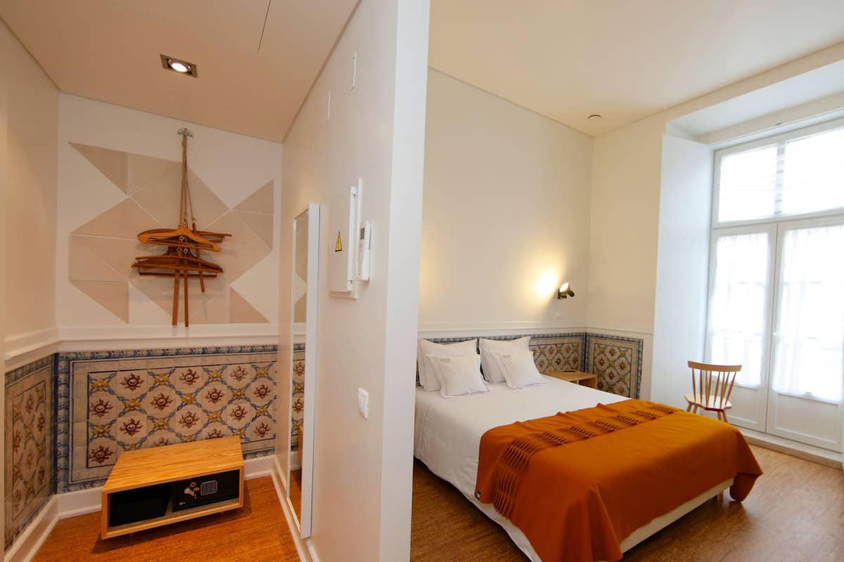 A bedroom with a bed, a wooden nightstand, a chair, and a small table with a radio.