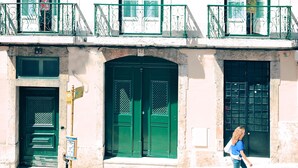Un bâtiment avec trois portes vertes, un balcon doté d’une rambarde en métal et un panneau de signalisation.