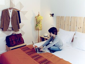 A hotel room with a bed, a laptop, a suitcase, and a coat rack with jackets. - Hall Chiado (Lisbon)