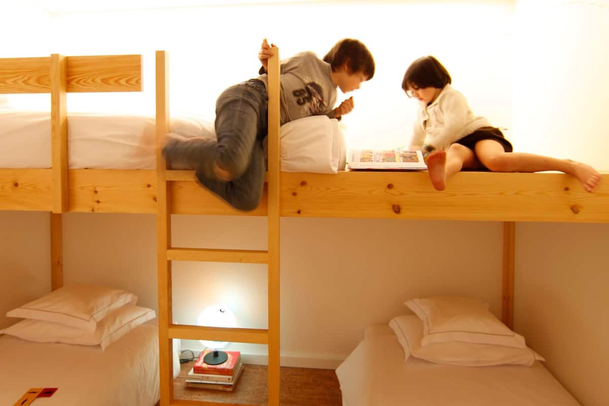 A bunk bed room with a ladder, two beds, and a small table with books.
