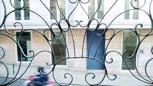 A metal fence with ornate designs in front of a building with a blue door and windows. - Hall Chiado (Lisbon)
