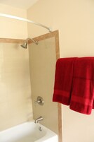 Un baño con una bañera blanca, una ducha con cabezal de ducha manual y una toalla roja colgada en un perchero.