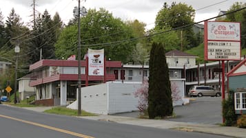 Un motel con fachada roja y blanca, un letrero que anuncia 'Old European Breakfast & Lunch', y un estacionamiento con un coche.