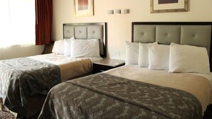 A hotel room with two beds, each with a headboard and pillows. There are framed pictures on the wall and a window with curtains. - American Travel Inn (Pullman)