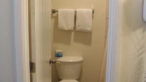 A small, narrow bathroom with a toilet, two white towels hanging on a rack, and a toilet paper holder. - American Travel Inn (Pullman)