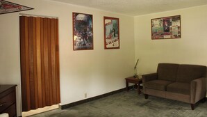 A living room with a brown sofa, a wooden door, and three posters on the wall. - American Travel Inn (Pullman)