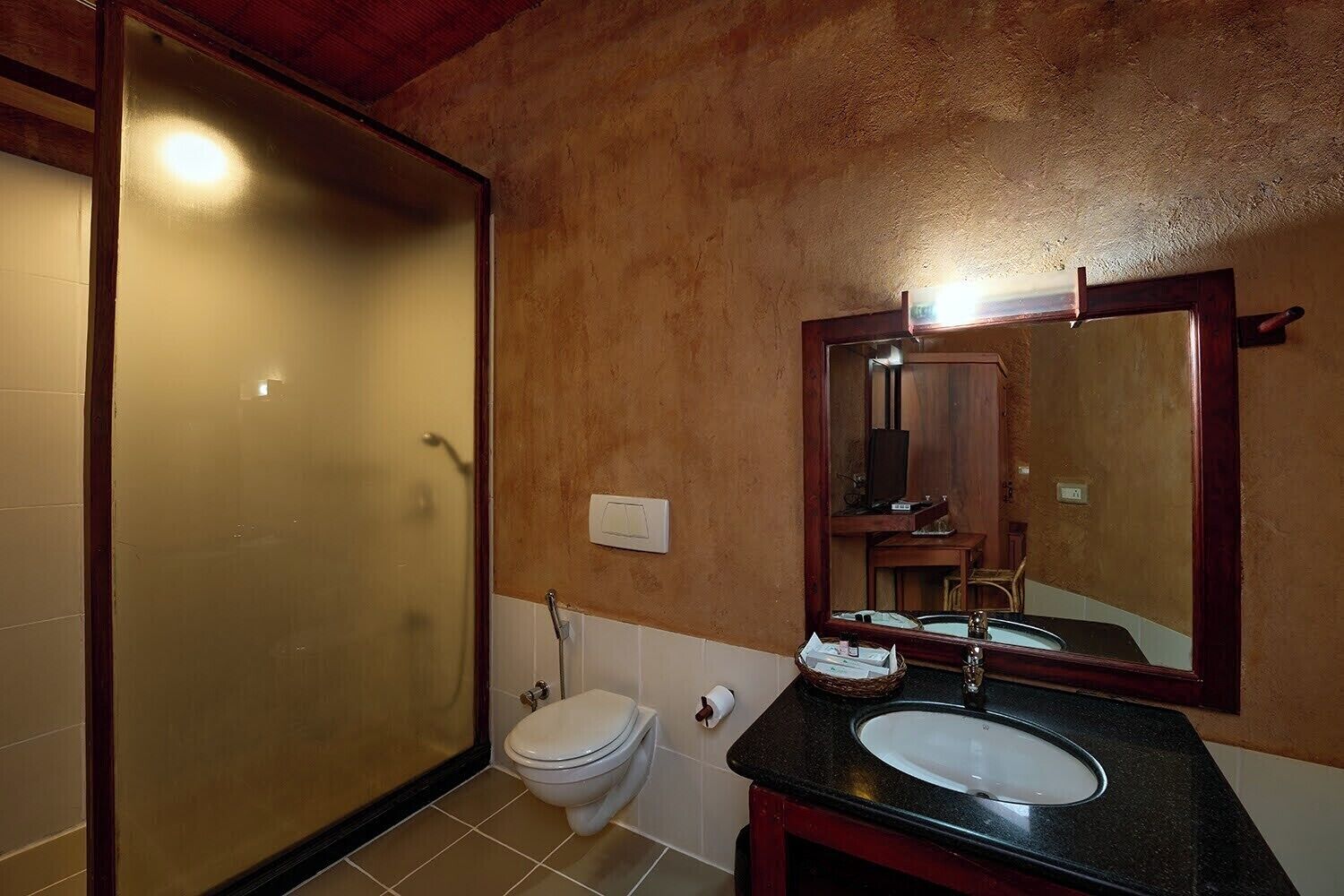 A bathroom with a glass shower enclosure, a toilet, a sink with a mirror above it, and a wooden vanity.