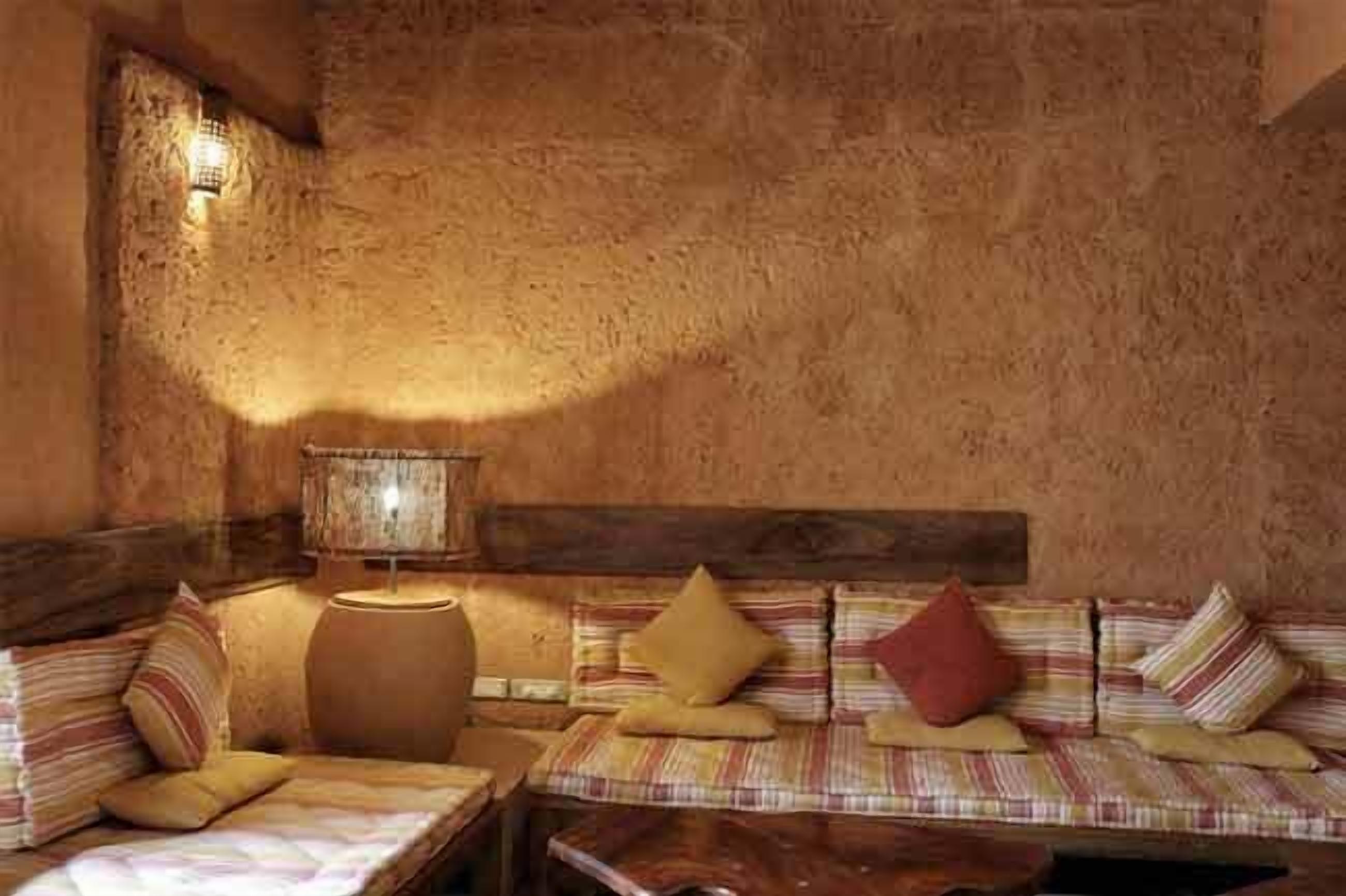 Una habitación rústica con un banco de madera y cojines, un barril de madera grande y una lámpara fijada a la pared.