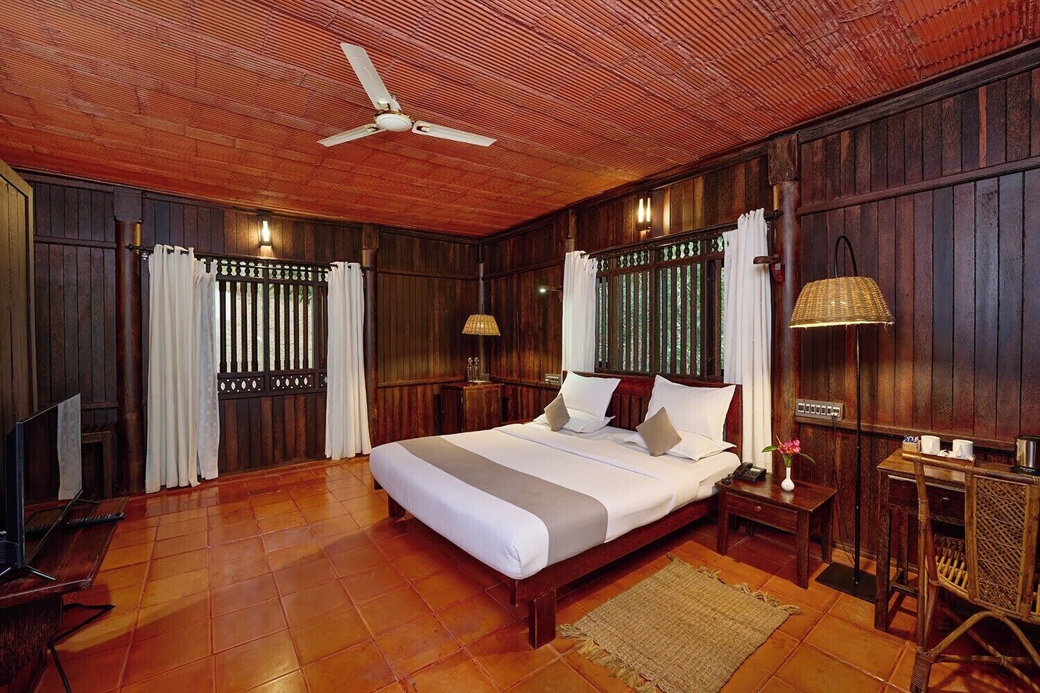 A wooden-paneled bedroom with a bed, a ceiling fan, a nightstand, a lamp, and a TV.