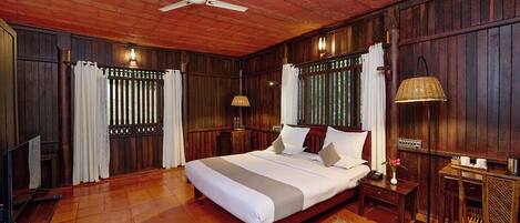 A wooden-paneled bedroom with a bed, a ceiling fan, a nightstand, a lamp, and a TV.