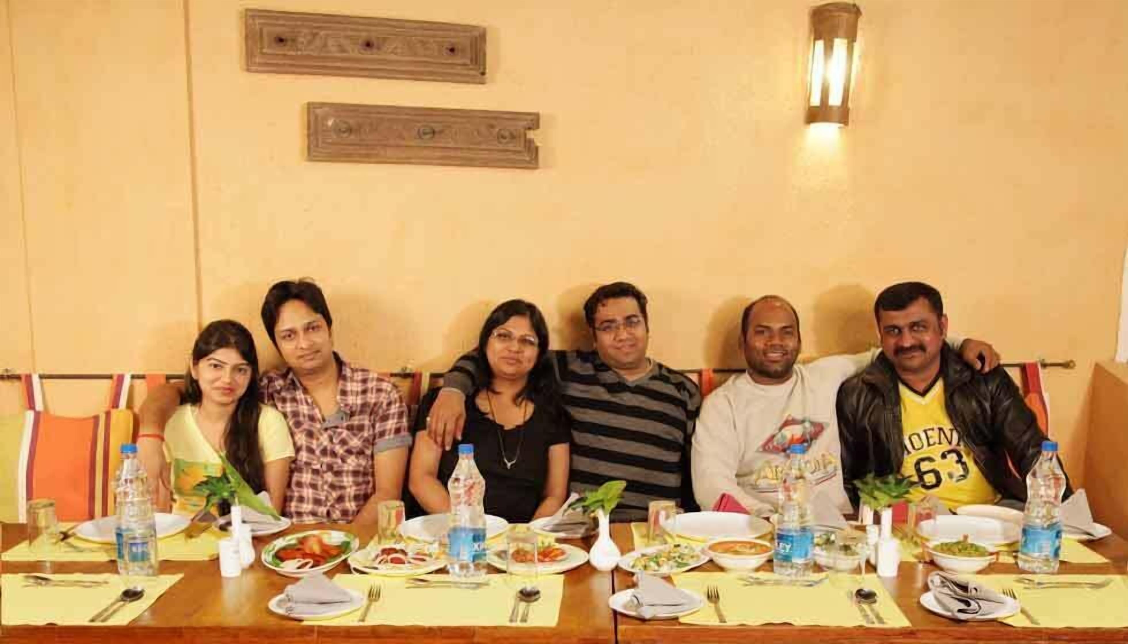 A group of people seated at a table with plates of food, water bottles, and a vase with a plant.