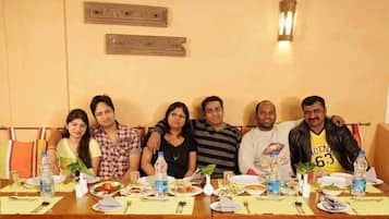A group of people seated at a table with plates of food, water bottles, and a vase with a plant.