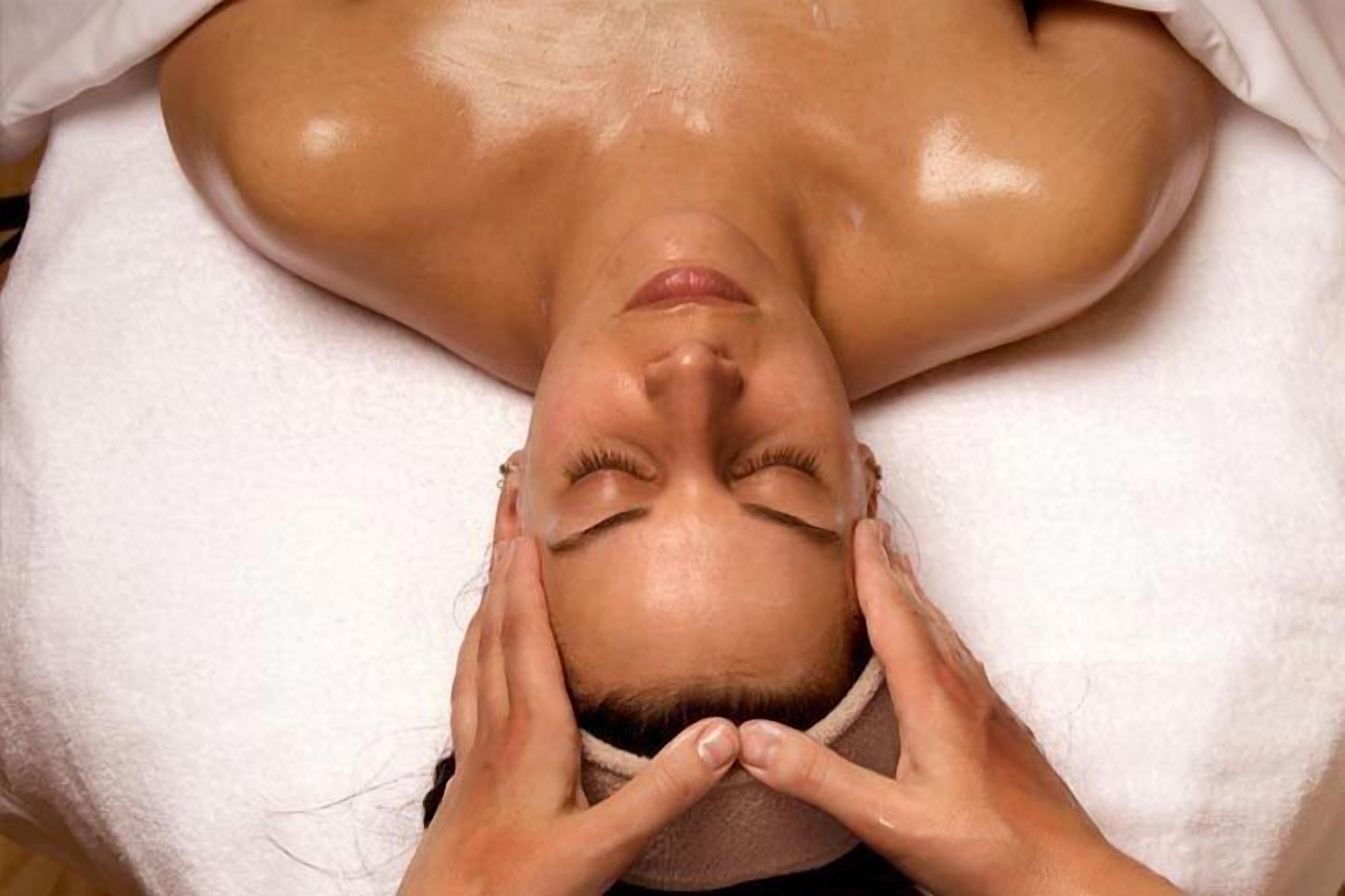 A person lying face down on a white towel, receiving a facial treatment.