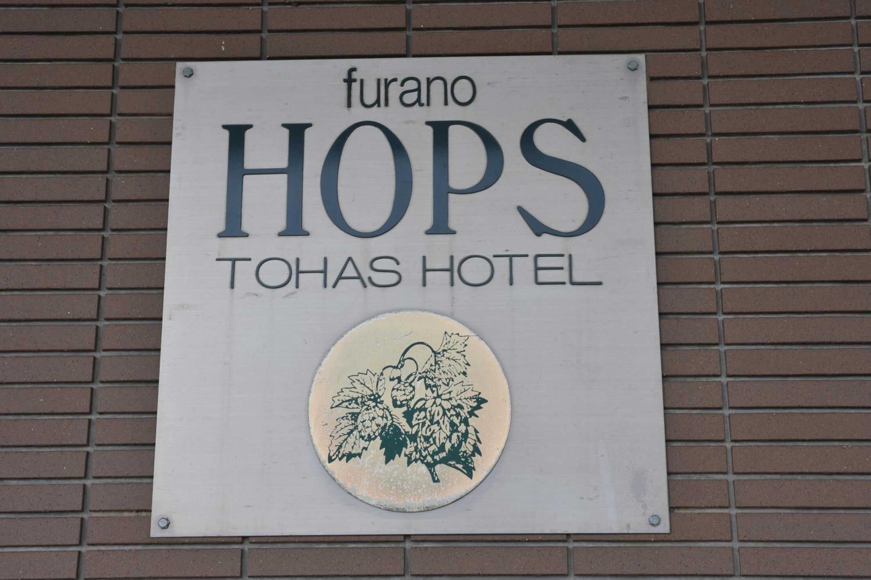 A sign for Furano Hops Tohas Hotel with a circular emblem of grapes.