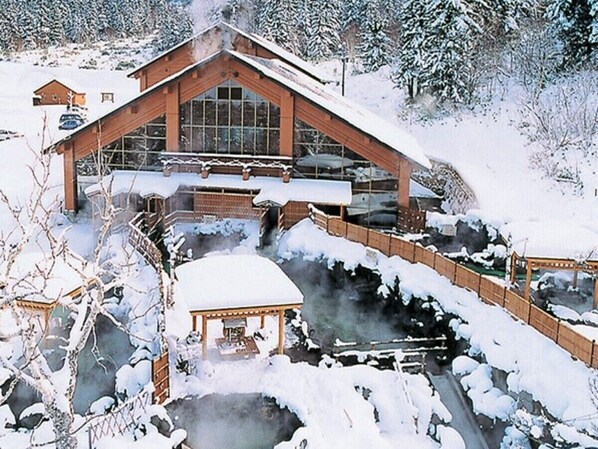 A wooden building with large windows, a covered area with a table, and a snow-covered landscape.