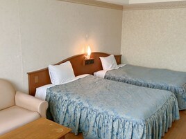 A hotel room with two beds, a wooden headboard, a nightstand, and a beige armchair.