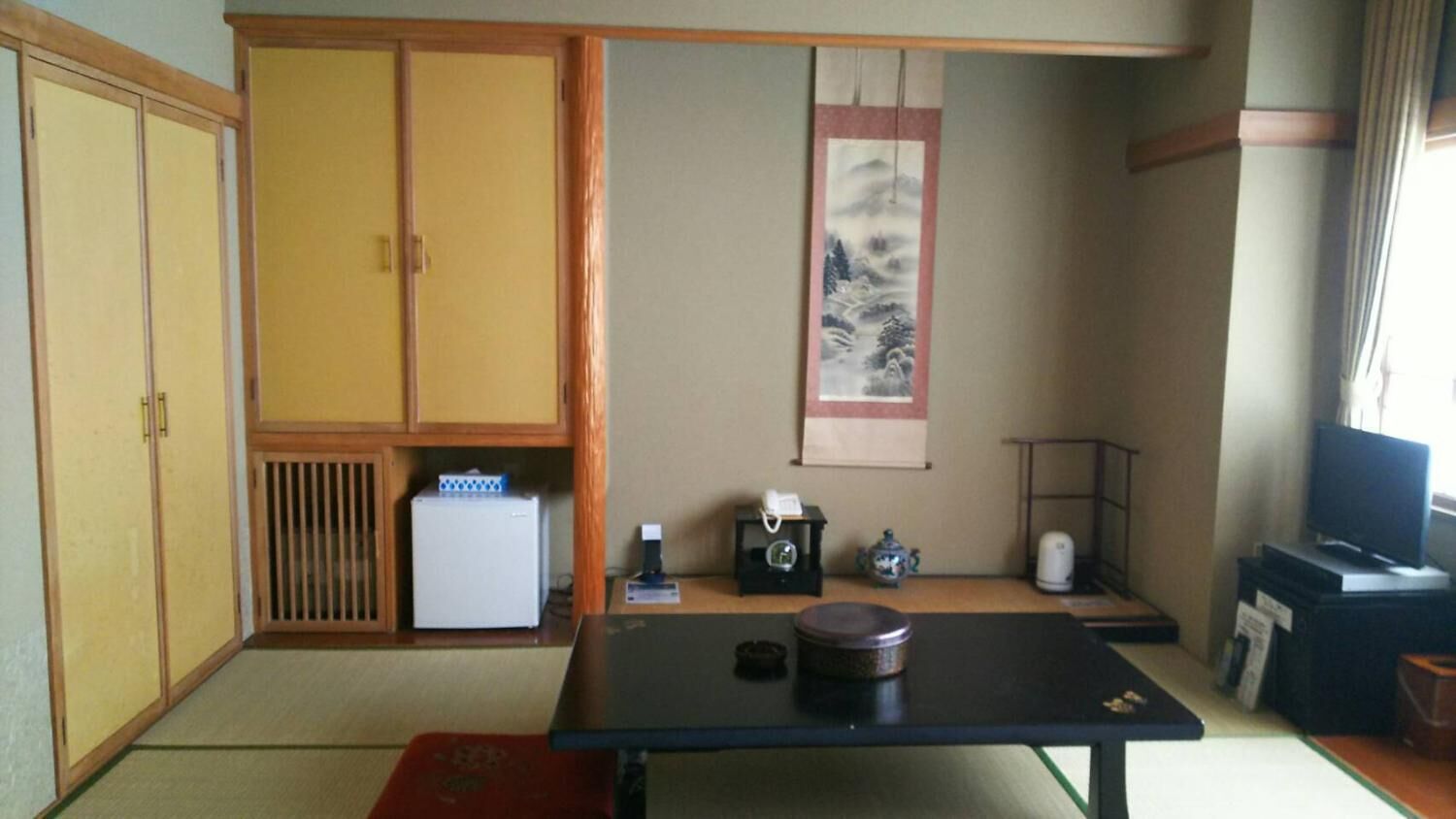Um quarto japonês tradicional, com tatames, uma mesa baixa, uma televisão e uma porta deslizante.