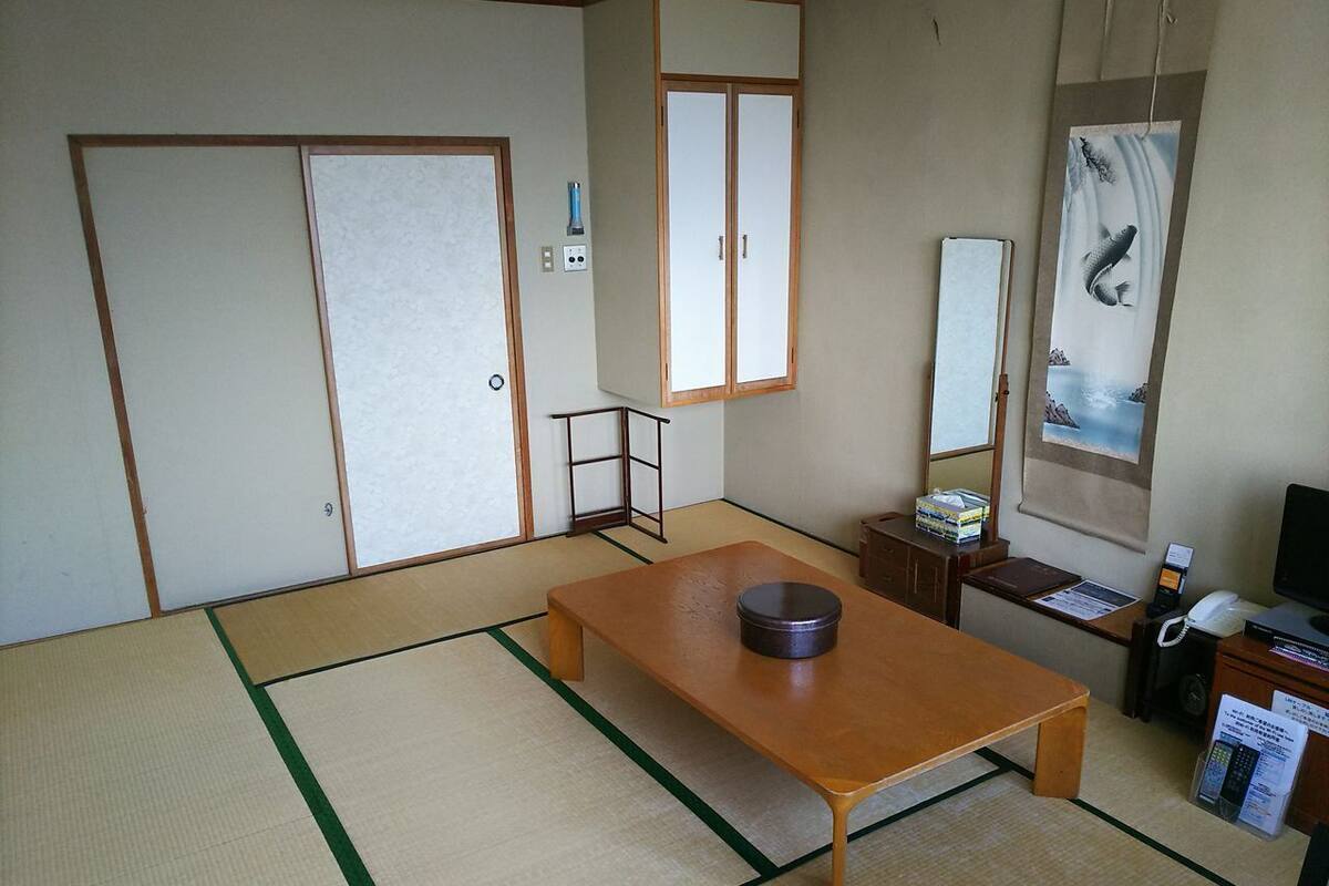 Una habitación japonesa tradicional con suelo de tatami, una mesa de madera baja, un escritorio con computadora y una puerta corrediza.