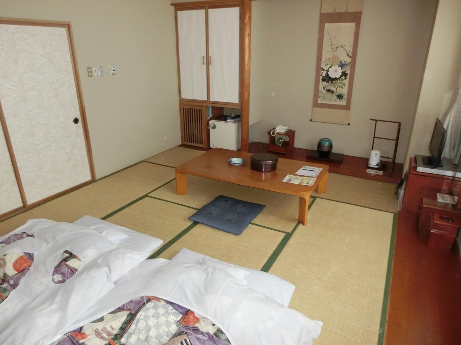 Una habitación japonesa tradicional con suelo de tatami, una mesa de madera baja, una cama con colcha colorida y una puerta corredera.