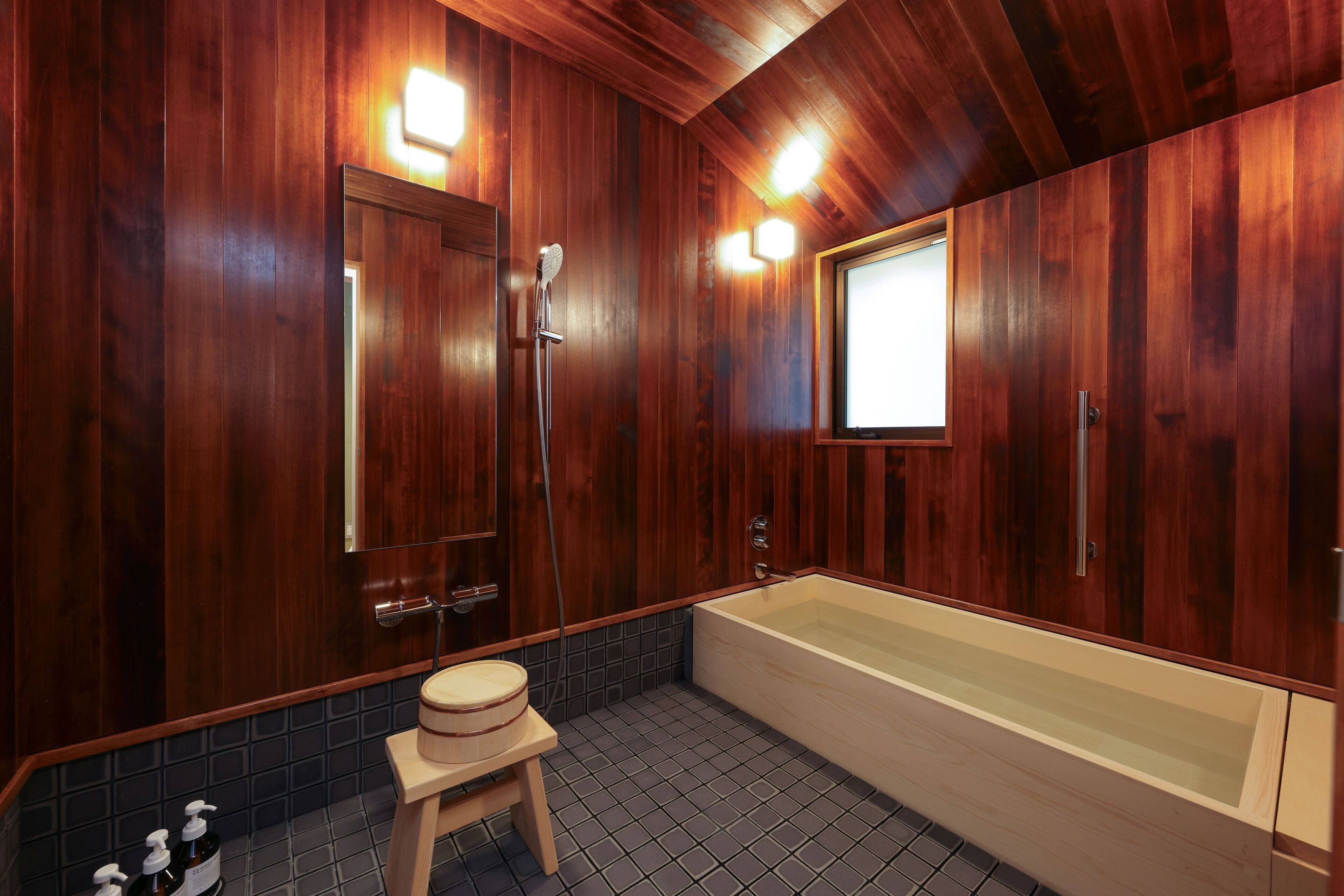A wooden-paneled bathroom with a bathtub, a wooden stool, and a mirror.