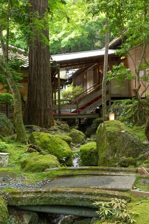 A traditional Japanese garden with a wooden walkway, moss-covered rocks, and a wooden structure with a staircase. - Nara Kasugaokuyama Tsukihitei (Nara)
