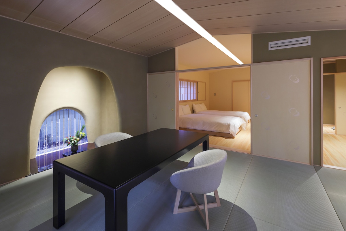 A modern hotel room with a large bed, a desk, and a chair. There is a window with a view of the outside.