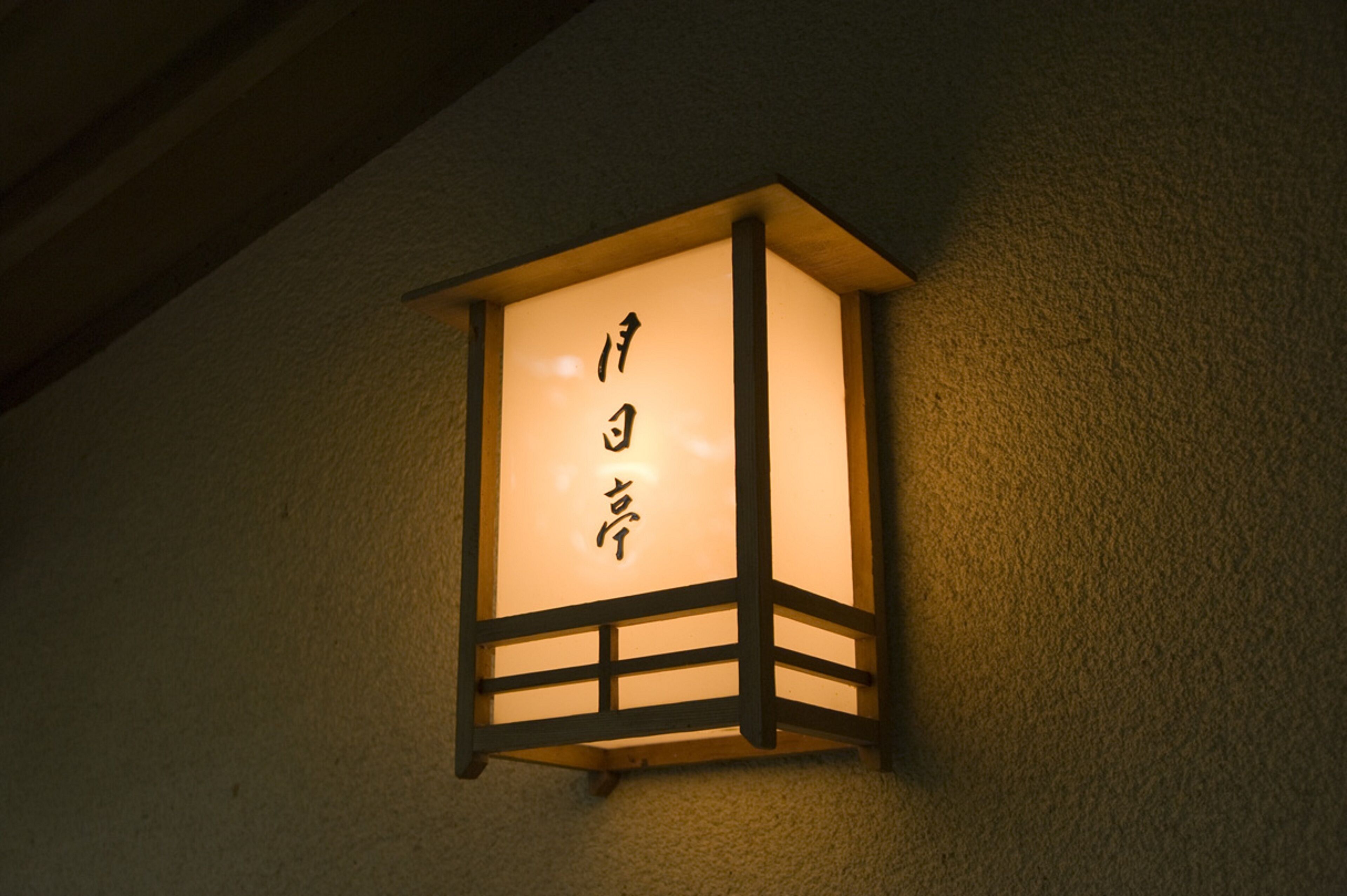 A traditional Japanese lantern with calligraphy on its panel, mounted on a wall.