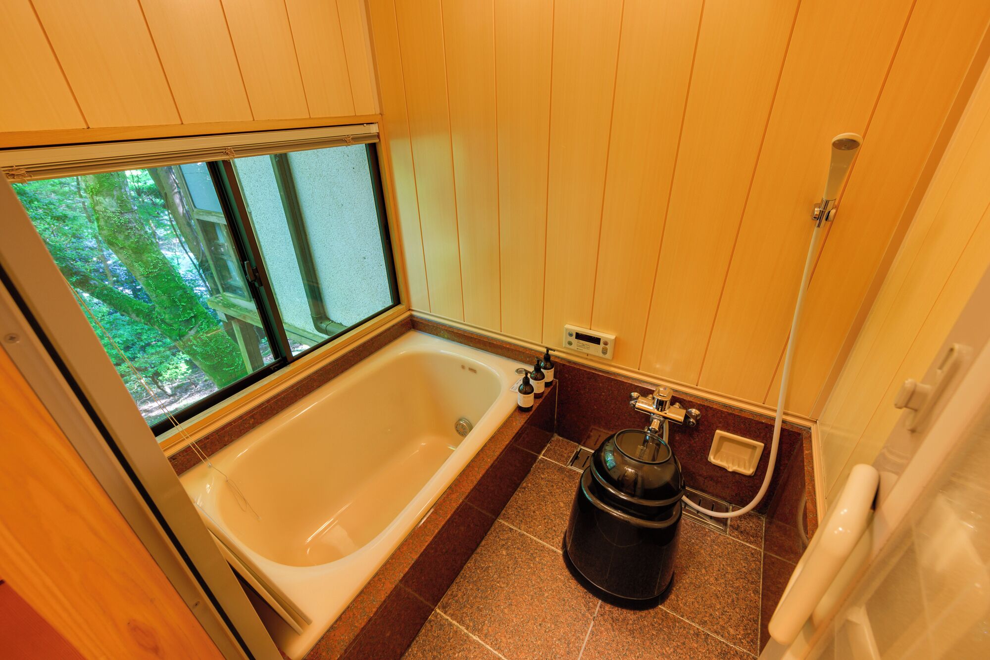 A bathroom with a bathtub, a shower, and a window with a view of trees.