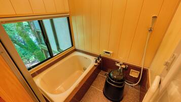 A bathroom with a bathtub, a shower, and a window with a view of trees.