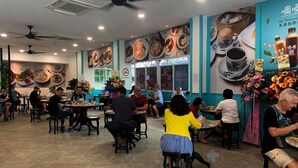 Interior de restaurante con varias mesas y sillas, ventiladores de techo y murales de comida en las paredes.
