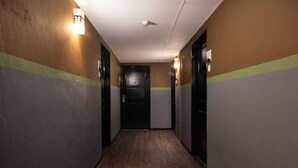 Un pasillo con piso de madera, paredes pintadas en tonos marrones y grises, y puertas negras con interruptores de luz.