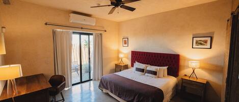 A hotel room with a bed, a desk, a chair, a ceiling fan, and a window with curtains.