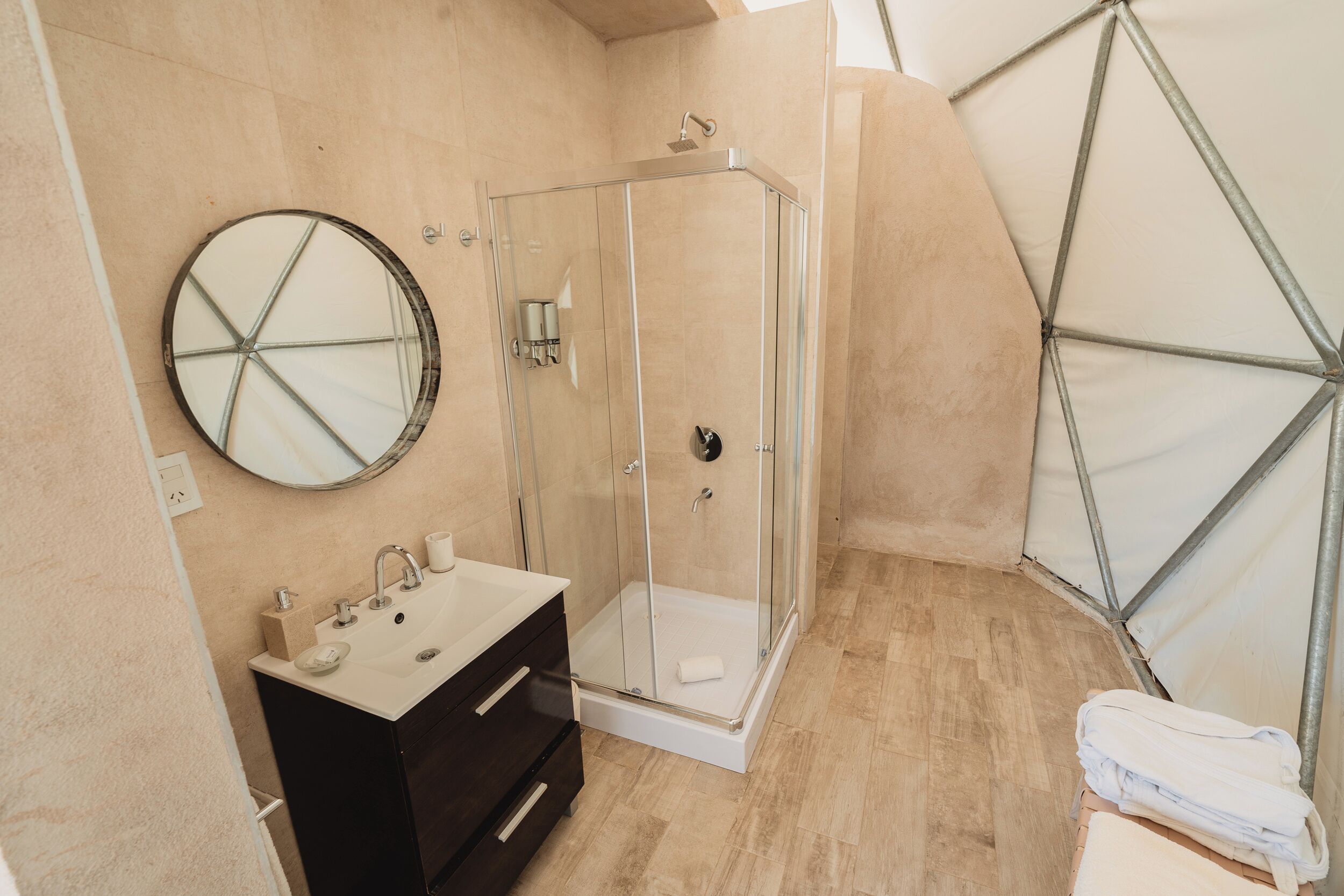 A modern bathroom with a glass shower enclosure, a round mirror, a sink with a black vanity, and a towel rack.