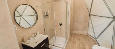 A modern bathroom with a glass shower enclosure, a round mirror, a sink with a black vanity, and a towel rack.