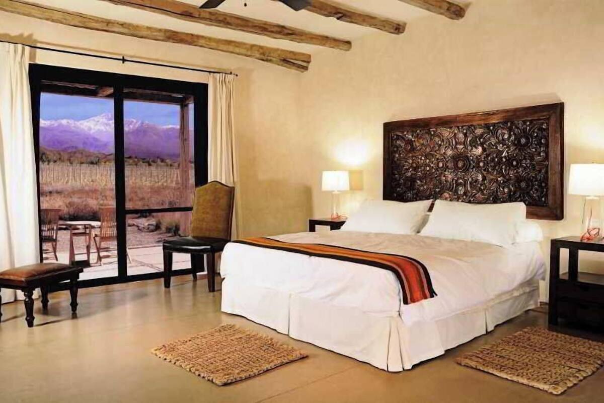 A bedroom with a large bed, a view of mountains through a sliding door, a wooden headboard, and two bedside lamps.