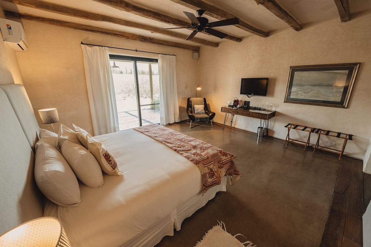 A bedroom with a bed, a desk, a chair, a ceiling fan, a TV, and a window with curtains.