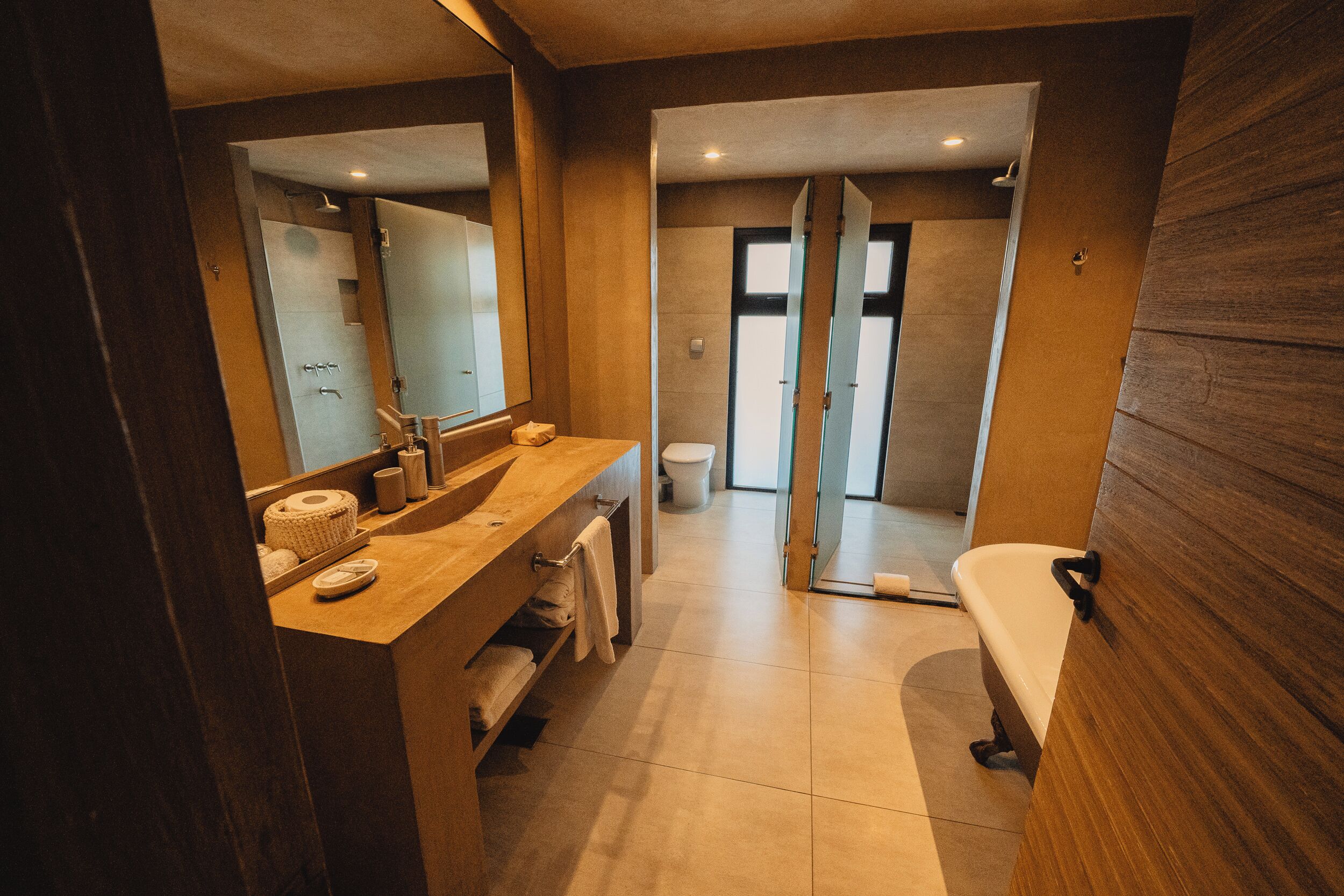 A modern bathroom with a wooden vanity, a large mirror, a toilet, and a shower area.