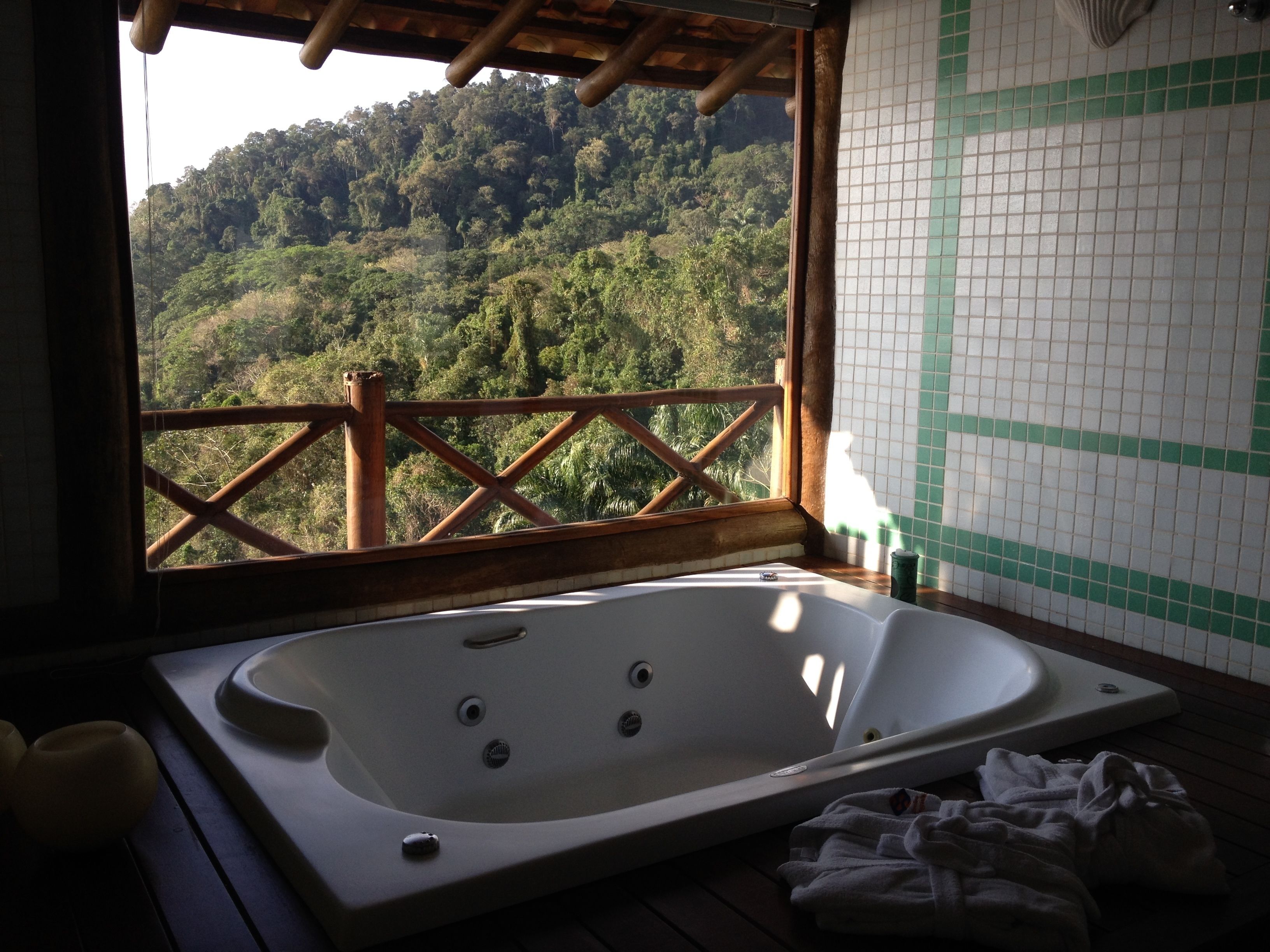 Une salle de bain dotée d’une grande baignoire, offrant une vue sur une colline boisée, et dont un mur est recouvert de carreaux avec une bande verte.