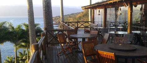 A wooden deck with tables and chairs overlooking a coastal view.