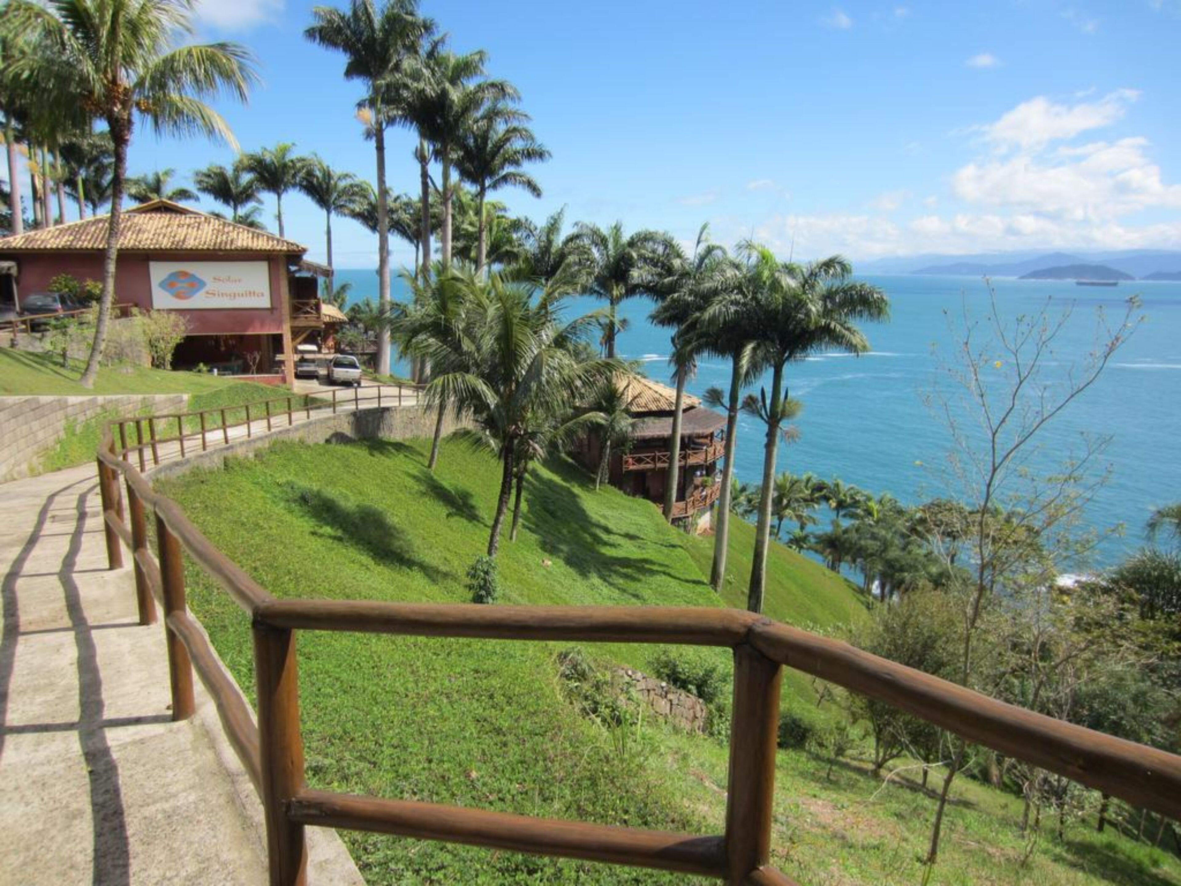 Ein Hotel an der Küste mit Meerblick, Palmen und einer Holztreppe zum Strand.