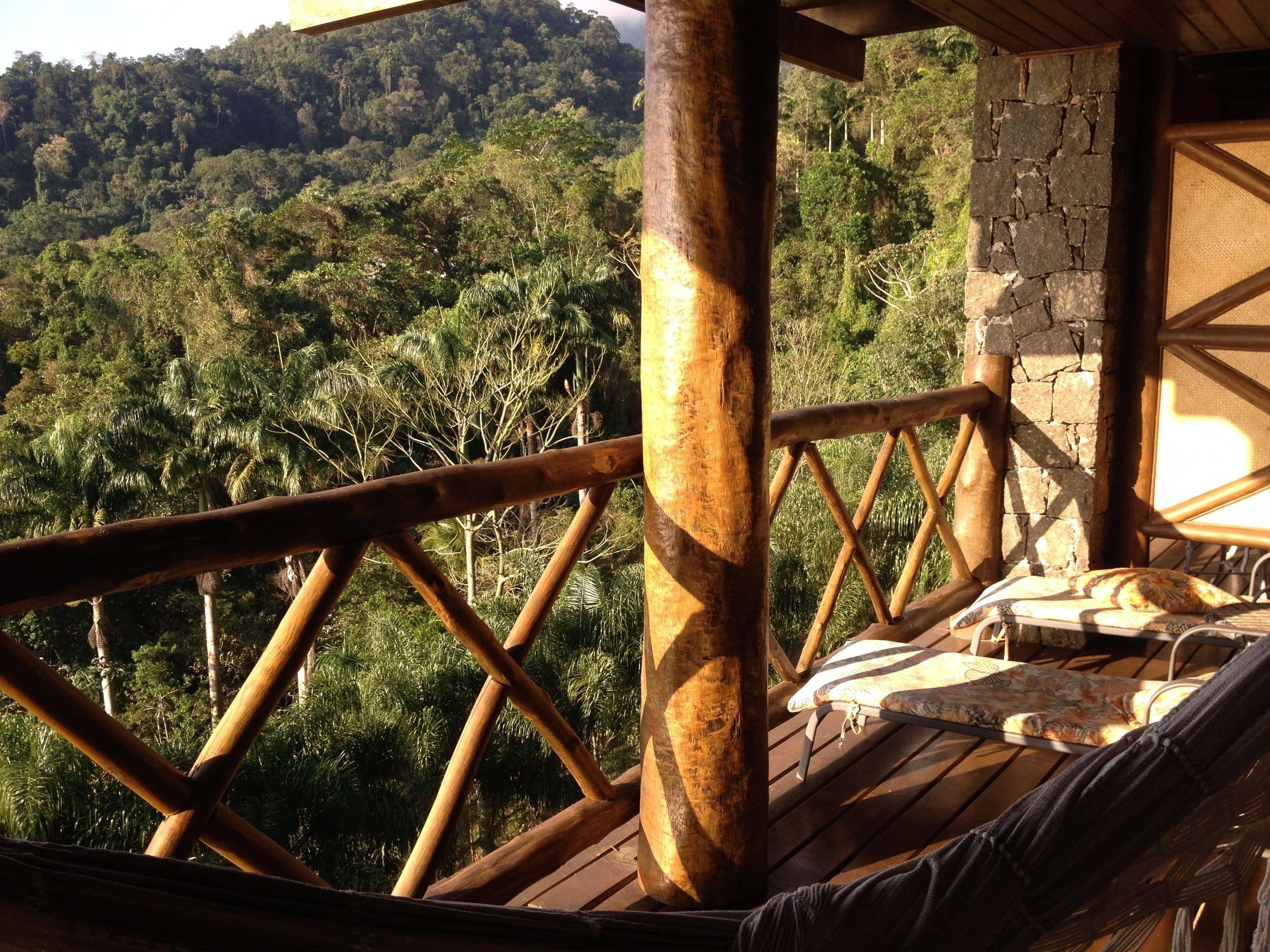 A wooden deck with a hammock and a stone wall, overlooking a dense forest.