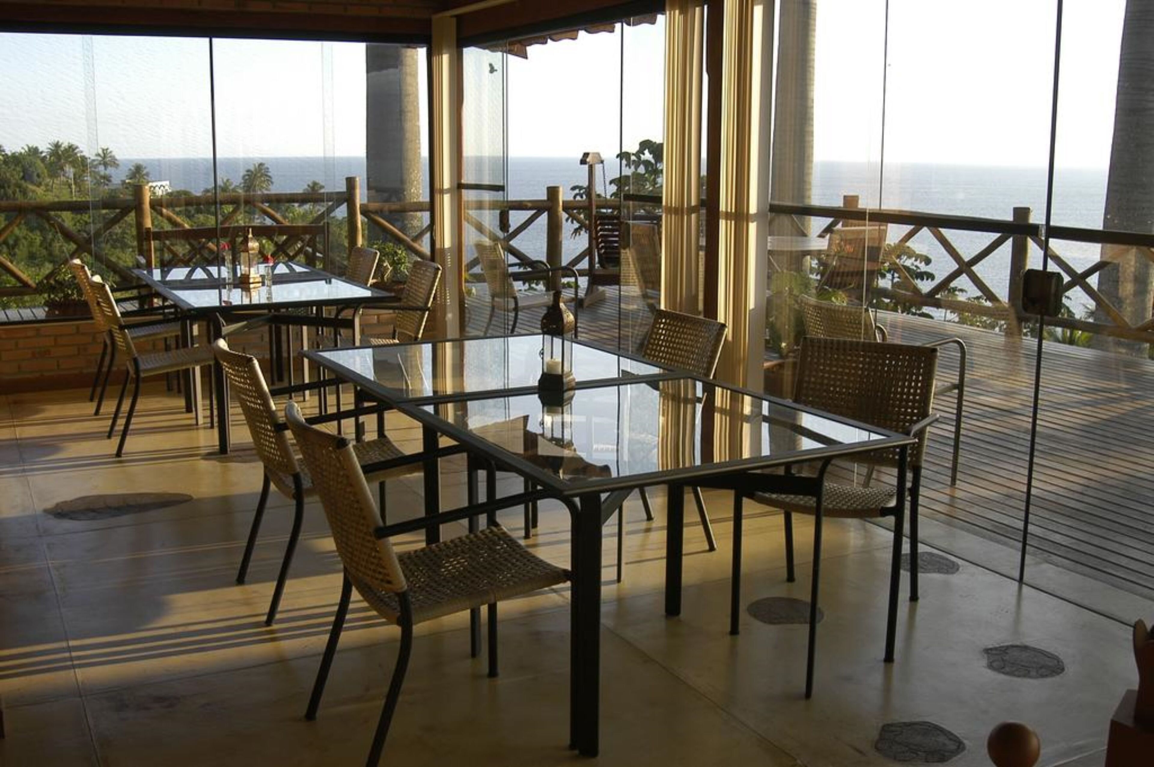 Una terraza con mesas de vidrio y sillas de mimbre, con vistas a la costa.
