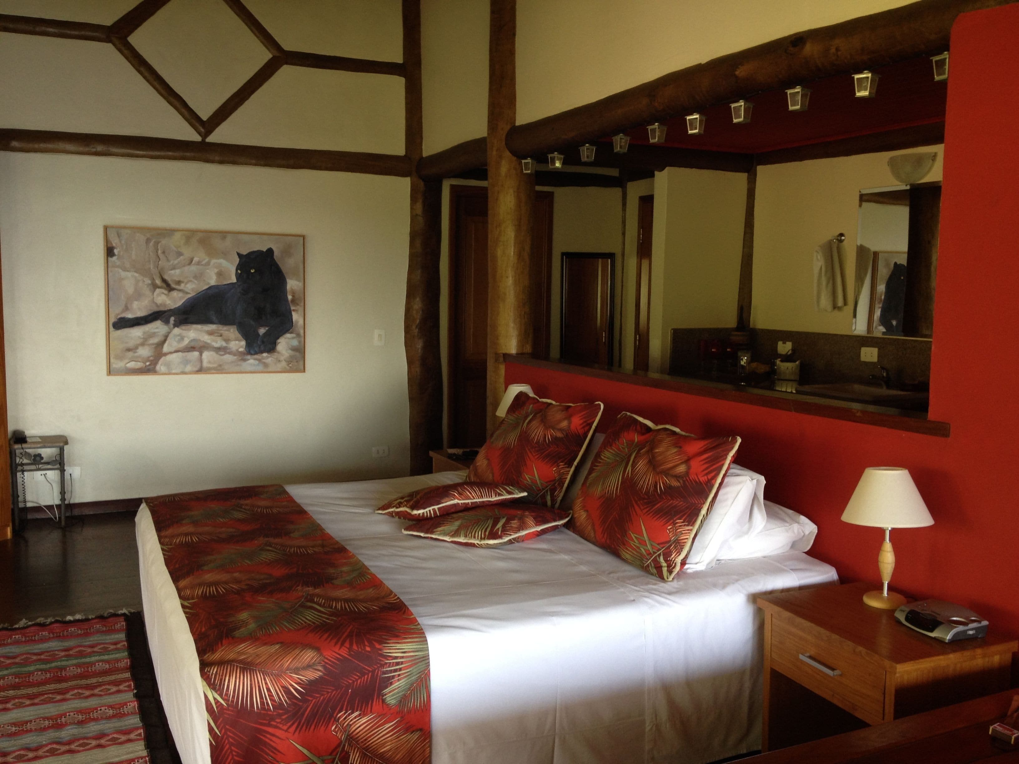 A hotel room with a bed, a nightstand, a lamp, a mirror, and a painting of a cat on the wall.