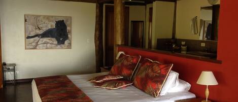 A hotel room with a bed, a nightstand, a lamp, a mirror, and a painting of a cat on the wall.