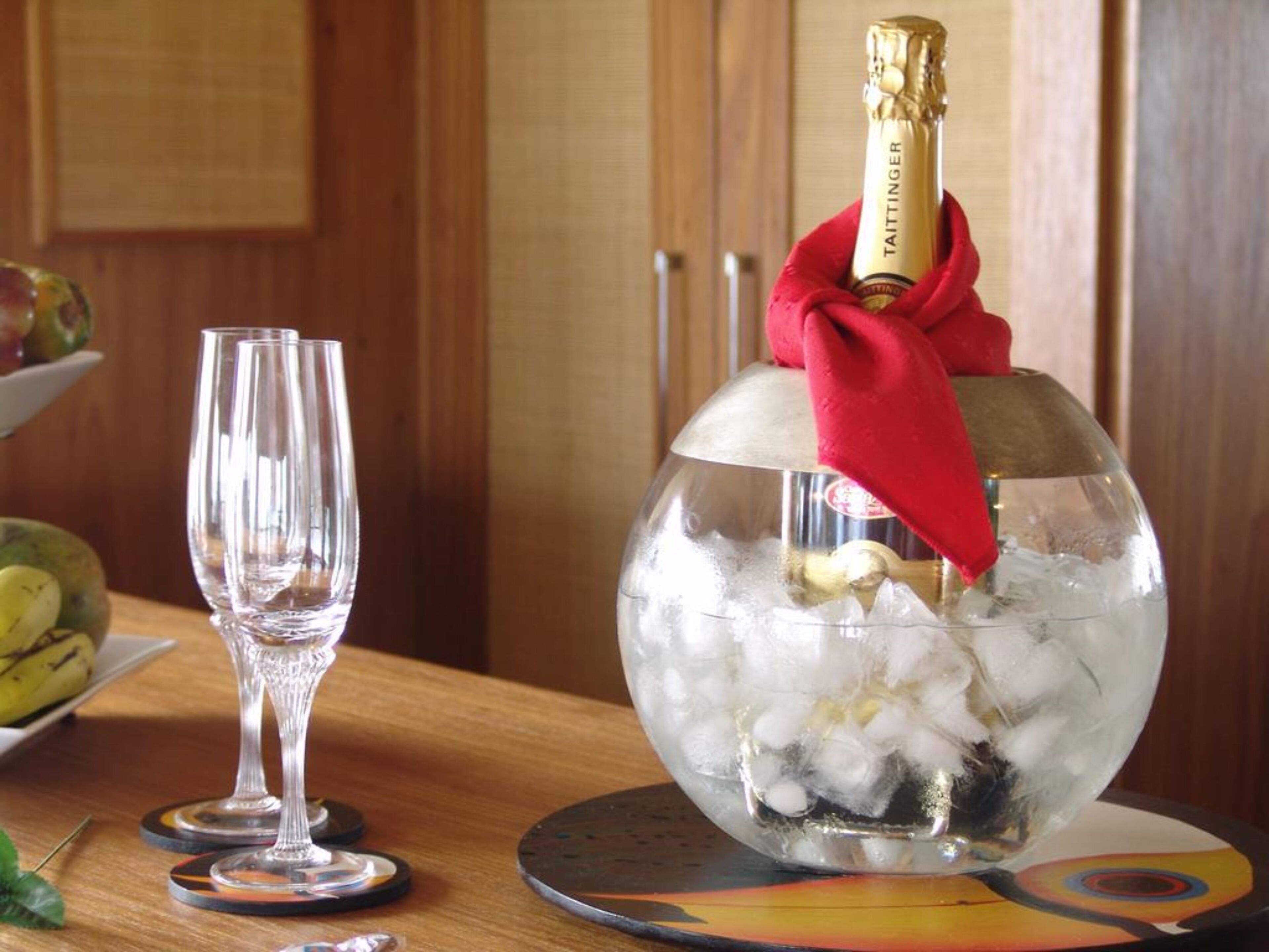 A glass bowl filled with ice and a bottle of champagne, placed on a coaster.