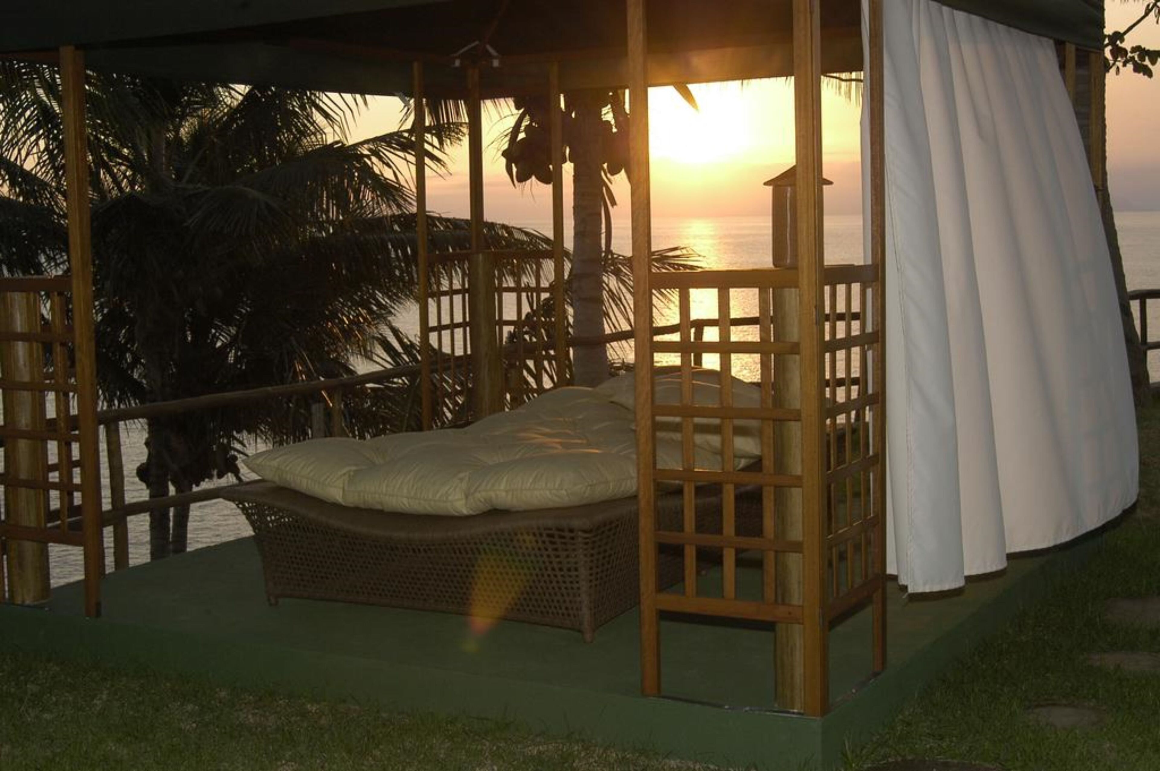 Un lit dans une structure en bois, avec vue sur le coucher de soleil sur l’océan.