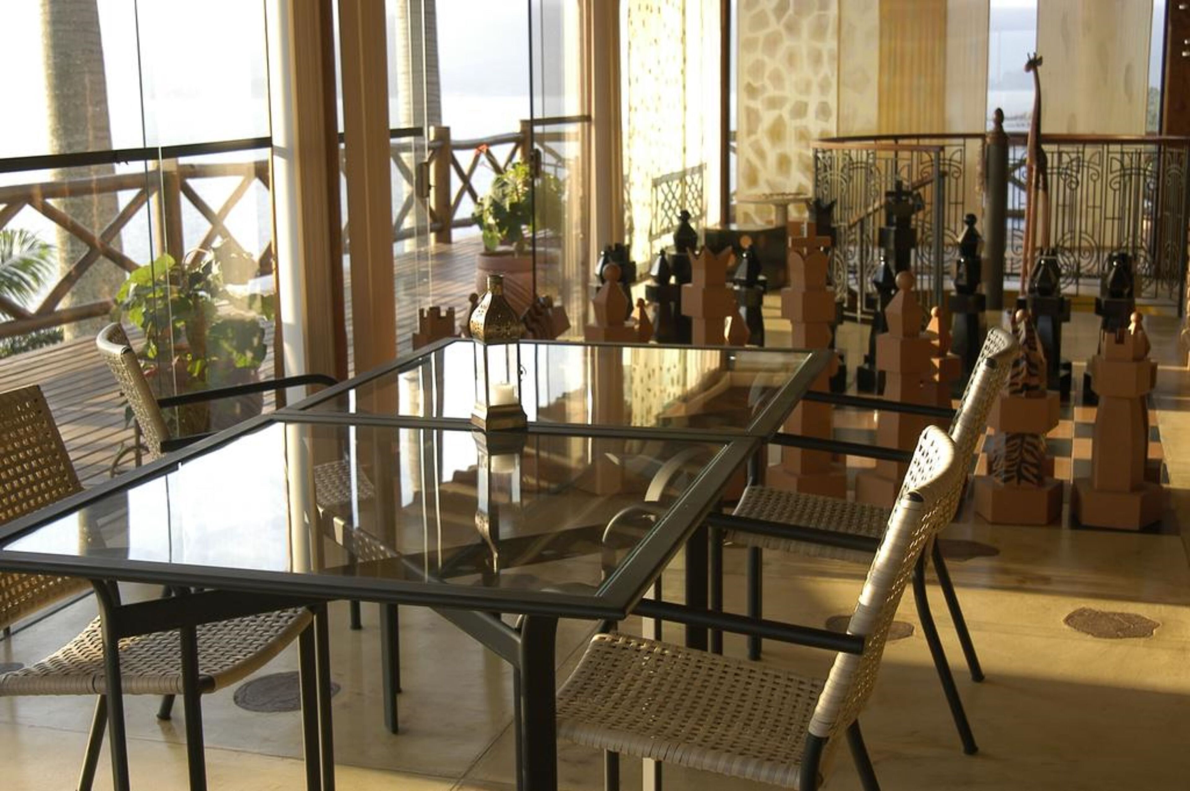 A spacious indoor area with a glass table surrounded by wicker chairs, a decorative railing, and potted plants.