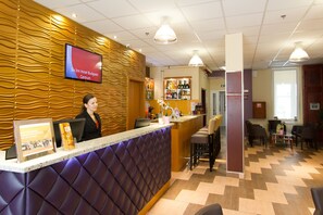 A hotel reception area with a modern design, including a reception desk, a bar area, and seating for guests. - Six Inn Hotel (Budapest)