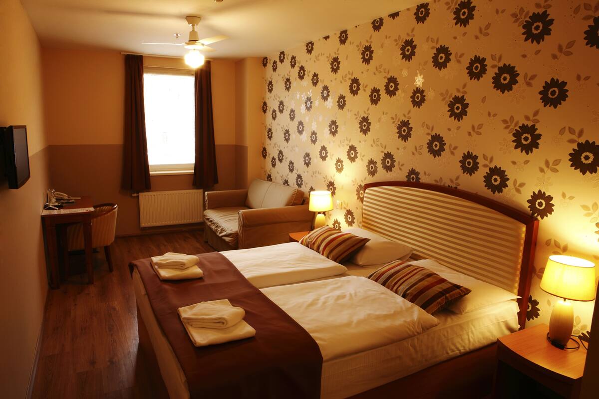 A hotel room with two beds, a desk, a chair, and a window with curtains.